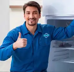 Técnico colombiano de ManteniCentro con uniforme oficial azul, sonriendo y dando el visto bueno tras completar la reparación de una nevera residencial en Cartagena.